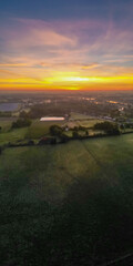 A mesmerizing aerial perspective capturing the stunning beauty of a dramatic dawn sky with vibrant colors transitioning from orange to pink to blue, casting a magical light over serene countryside