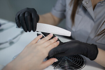 Manicure treatment at nail salon, master working and doing manicure with nail file