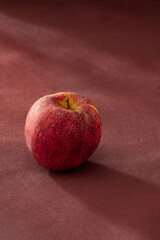 Roter Apfel mit Tautropfen auf Bordeauxroten Untergrund mit Struktur in herbstlicher Stimmung