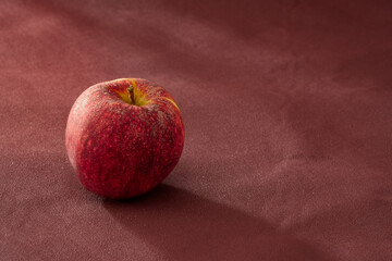 Roter Apfel mit Tautropfen auf Bordeauxroten Untergrund mit Struktur in herbstlicher Stimmung...
