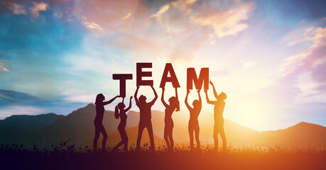 People, women and men holding TEAM word together at sunset, teamwork concept