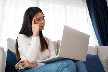 Young asian woman working on computer laptop on couch in living room at home