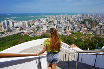 Fototapeta na wymiar Holidays in Brazil. Back view of beautiful fashion girl enjoying view of the Vitoria metropolitan region, Espirito Santo, Brazil.