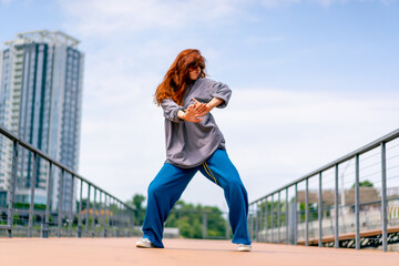 young red-haired street hip-hop dancer in sportswear dances impromptu dance us bridge attract the...