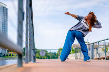 young red-haired street hip-hop dancer in sportswear dances impromptu dance us bridge attract the attention of passers-by hobbies active lifestyle - obrazy, fototapety, plakaty