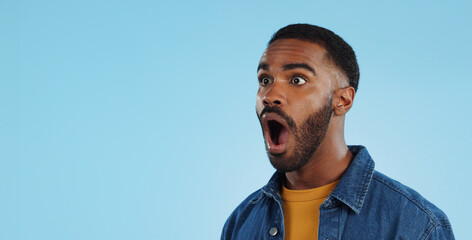 Black man, surprise announcement and shock on face, expression and drama on blue background. Wow,...