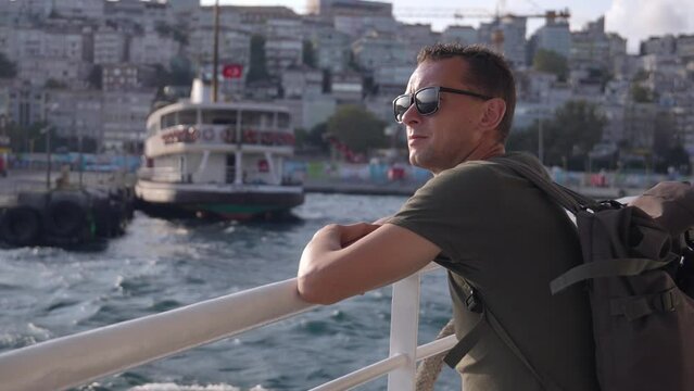 Young handsome man in sunglasses on ferry in istanbul resting on bosphorus. Guy traveler with backpack on ship. Boat. Waves in background. Sightseeing by boat around city