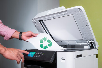 office worker prints paper on a multifunction laser printer with recycled paper in home office...