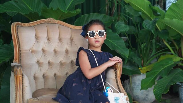 Cute girl wearing sunglasses sitting on counch against the plant.