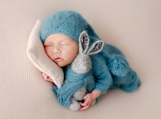Adorable newborn baby boy sleeping with bunny toy wearing knitted hat and clothes. Cute infant child kid napping on pillow