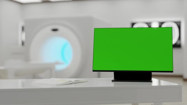 In the foreground, there's a table with a computer turned on, showing a green screen on the monitor. In the background, there's a blurred MRI room.Hospital room with tomograph. The light turning on.