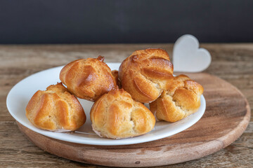 Profiteroles or cream puff or choux pastry balls on wooden background.