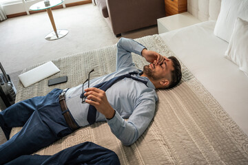 The businessman enters his hotel room, with a sense of relief, sinks onto the hotel bed. The comfort of the room offers a well-deserved moment after a long day of meetings. - 662795671