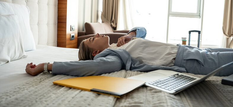 The businesswoman enters her hotel room and, with a sense of relief, sinks onto the hotel bed. The comfort of the room offers a well-deserved moment after a long day of conferences and meetings.