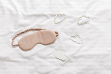 Sleeping mask beige color and clouds shapes on bed white bedclothes background. Eye cover for best sleep. Creative Concept of dream well and good night, comfort rest at night. Top view