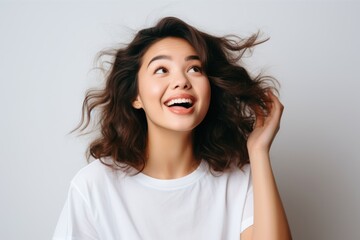 Beautiful young girl with curly hair in white t-shirt cheerfully smiling over grey background. Happiness. Human emotions