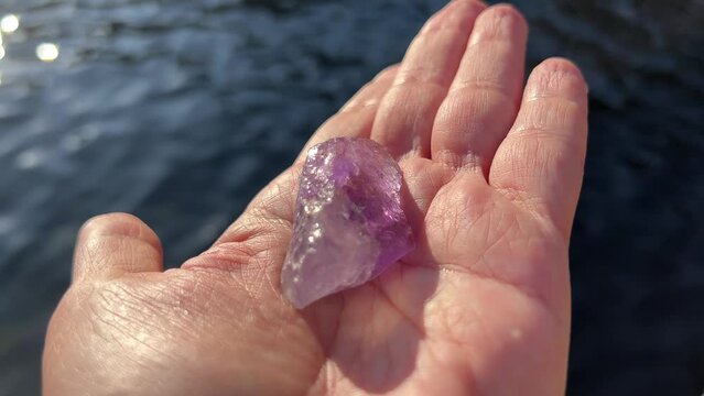 Hand holding purple stone amethyst citrine bolivianite against clear water.