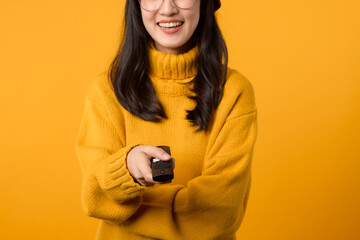 A young Asian woman in a yellow sweater relaxes on her couch with a remote control, indulging in some weekend entertainment.