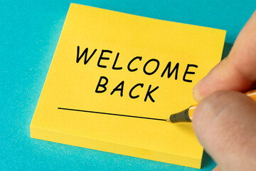 Paper notes with the words Welcome Back ON YELLOW STICKY PAPER NOTE AND BLUE BACKGROUND on a gray...