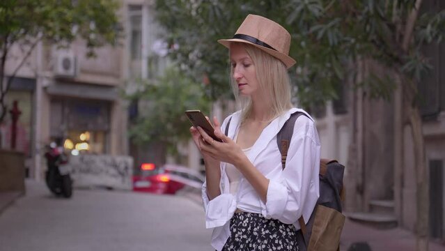 Female tourist in saloon hat and ryuukzakom studying app in smartphone. Maps of city or calling taxi, hotel. Finding accommodation, app concept or travel software. Joyful Tourist