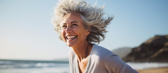 Enthusiastic middle aged lady enjoying leisure at the shoreline With copyspace for text - obrazy, fototapety, plakaty