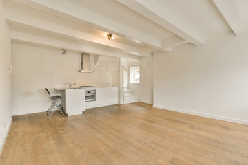 an empty living room with wood flooring and white paint on the walls there is a kitchen in the corner