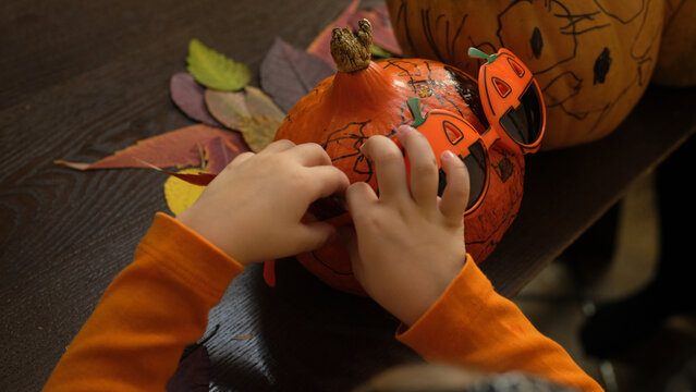 side view of cute child in witch costume painting pumpkins for halloween at home