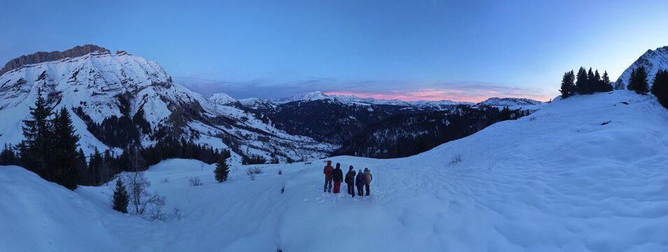 Panorama of a group of friends on a snowy hill in front of a mountain pass at sunset