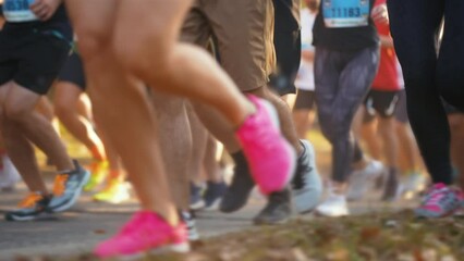 Bottom view crowd of people wearing sportswear running on roadway in sunshine morning. Legs view of runners at autumn city marathon . Healthy lifestyle. Concept of sport