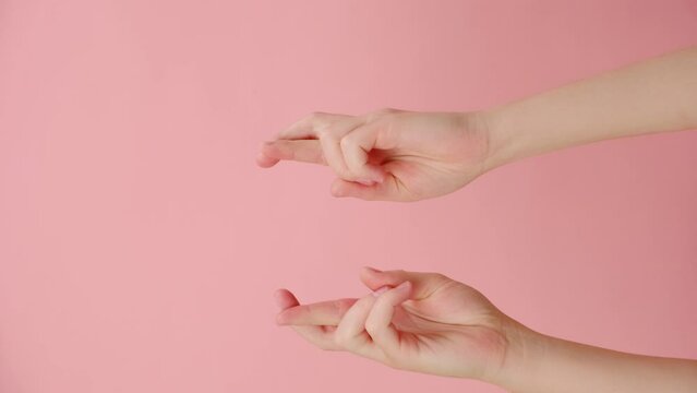 Vertical video of female hands praying with crossed fingers hopes for miracle good outcome, isolated over pink background with copy space. Body language concept. Advertising area, workspace mock up