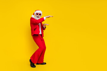 Fototapeta na wymiar Full length photo of cheerful cool claus wear red tux costume having fun measuring arms empty space isolated yellow color background