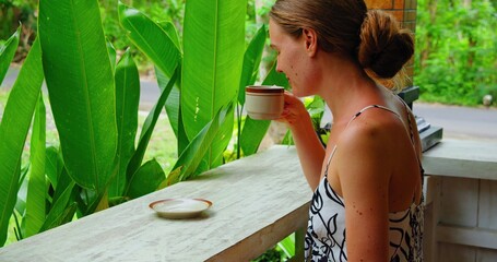 Girl smells and drinking hot morning Balinese coffee enjoying green tropical garden nature. Side...