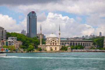 Dolmabahce Camii Mosque with Suzer Plaza building at the background at Bosporus strait waterside in Beyoglu district in historic city of Istanbul, Turkey. 