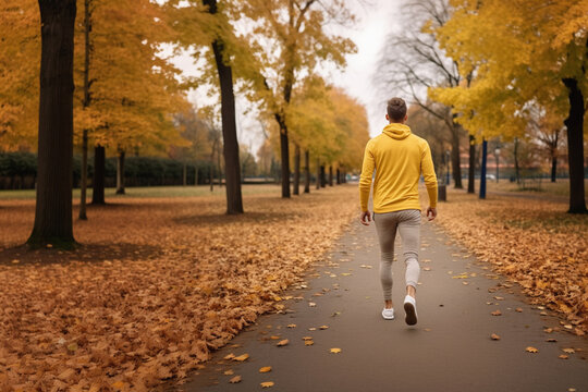 Rear view of young man walking, exercising and running on the street in the park on an autumn morning. Concept of health and lifestyle.