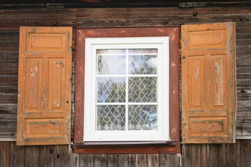 Wooden window rustic cottage house. Vintage wall with transparent glass window and decorative brown shutters. Countryside architecture historic building. PVC white window. Village house.