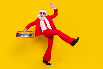 Fototapeta na wymiar Full length photo of good mood claus wear red tux costume listening boom box walking empty space isolated yellow color background