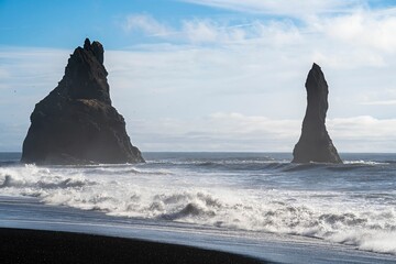 blacksand beach in Iceland with two basalt toweing rocks in the sea