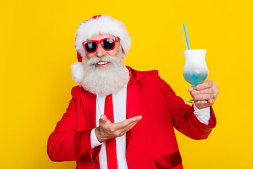 Photo of cheerful cool senior guy wear x-mas suit recommending enjoying tasty beverage isolated yellow color background