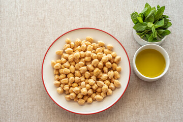 Chickpeas in ceramic plate, fresh mint, olive oil on cotton fabric background. Ingredients for cooking.