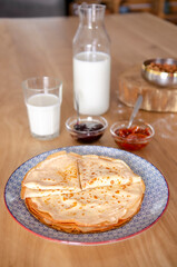 Sweet round pancakes lying on a round plate next to jam