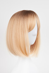 Fototapeta premium Natural looking blonde fair wig on white mannequin head. Short hair cut on the plastic wig holder isolated on white background, side view.