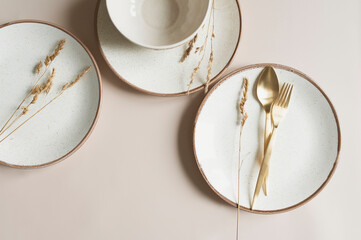 beige empty porcelain plate on pastel background with golden cutlery and dried flowers. Boho...