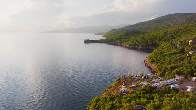 Beautiful sunset at the Adriatic coast in Croatia. Aerial flight over hilly land with forests and some campers at the coastline. 