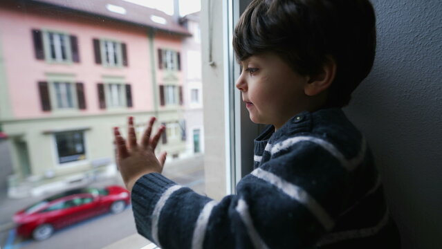 Child breathes into home window creating condensation, bored kid locked indoors breathing into glass from second floor building