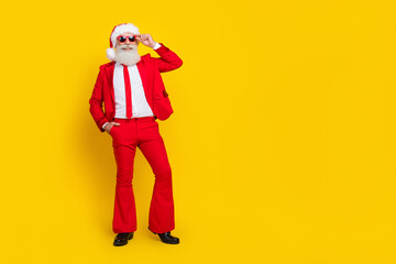 Fototapeta na wymiar Full length photo of cheerful attractive retired guy wear red tux claus hat arm hand dark eyewear empty space isolated yellow color background