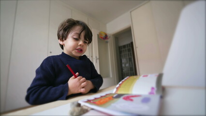 Creative Child preparing to draw, picking coloring pen from inside desk drawer, sititng down in bedroom concentrated to do school kindergarten study