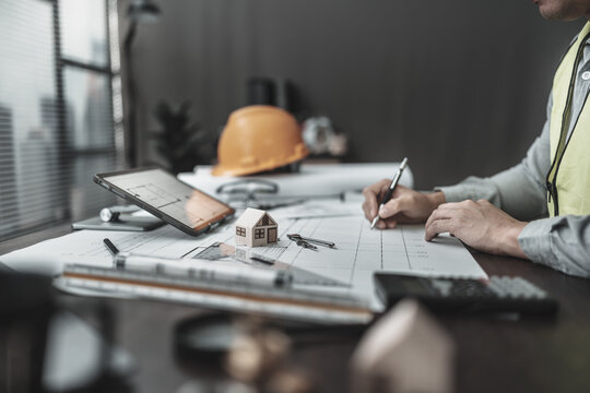  mini house model   in frot of Architect engineer working on blueprint. Protect House, cost planning design and construction concept.