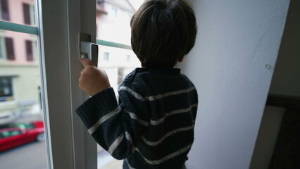 Child holding into window knob. Danger concept of small boy near glass from second floor apartment residence