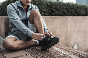 A man tying shoelaces on sport shoes in the city center park before cardio workout, running. ...