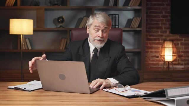 Displeased aged male in business attire taking off spectacles while shutting off laptop monitor in frustration at work. Annoyed general manager taking break from disappointing online conversation.
